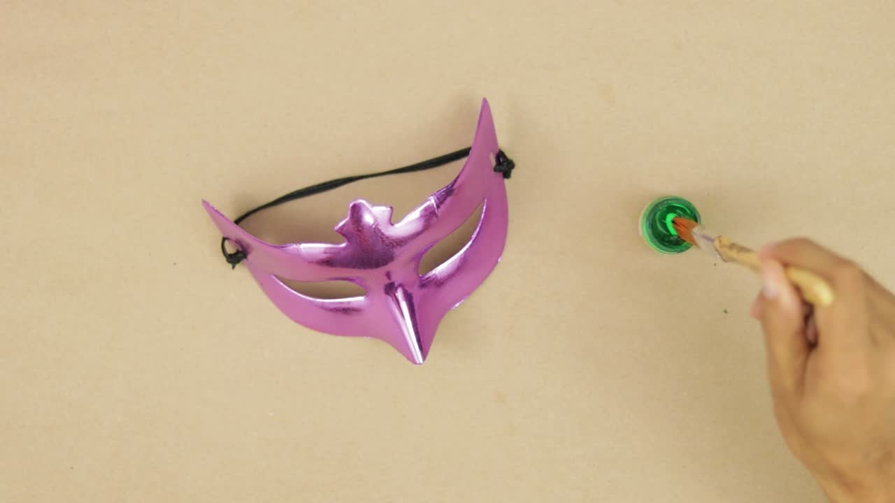 손은 질과 녹색 페인트로 카니발을 위해 크롬 눈 마스크를 칠합니다.