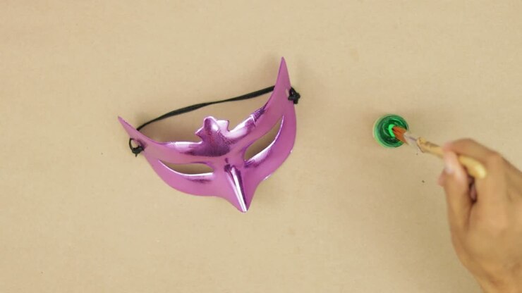 Hands painting a chrome eye mask for carnival with a brush and green paint