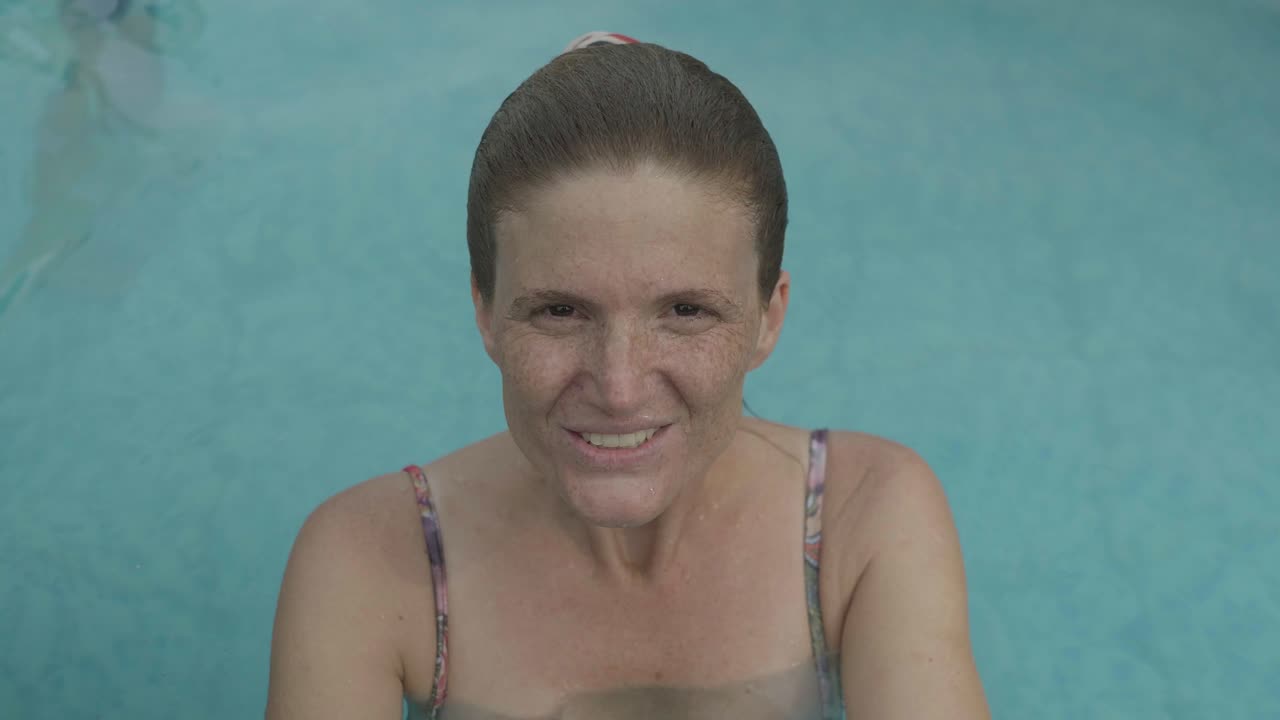 una joven pelirroja sonríe a la cámara desde el interior de una piscina