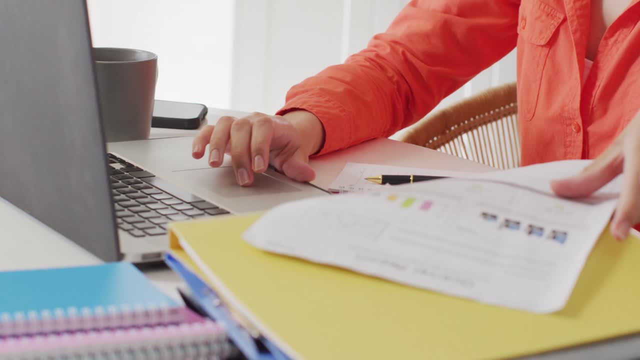 mujer biracial sentada en la mesa y trabajando con una computadora portátil