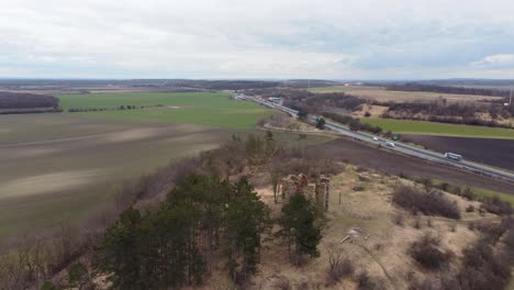 aerial-shot-of-old-ruins-on-a-hill-with-a-highway-behind-it,-cloudy