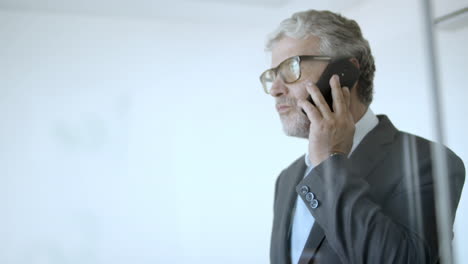 serious mature executive in suit walking in his office and talking on the phone