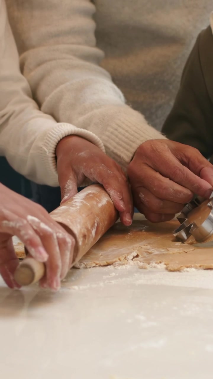 Vertical video: Retreating hands, baker in sweater rolling dough on home bench with pin for cookies