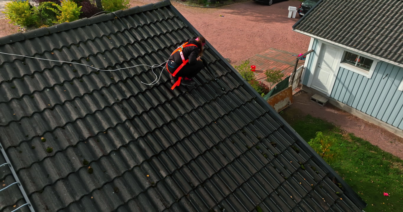 Aerial view of a woman cleaning house roof tiles, on a sunny, autumn day