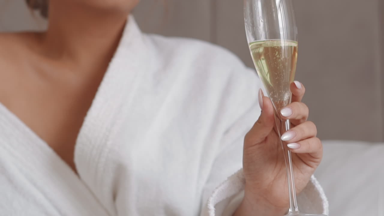 Giovane donna con indosso un accappatoio bianco tiene in mano un bicchiere di champagne