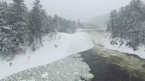 drone flying thru snowfall towards magical winter scenery of a waterfall