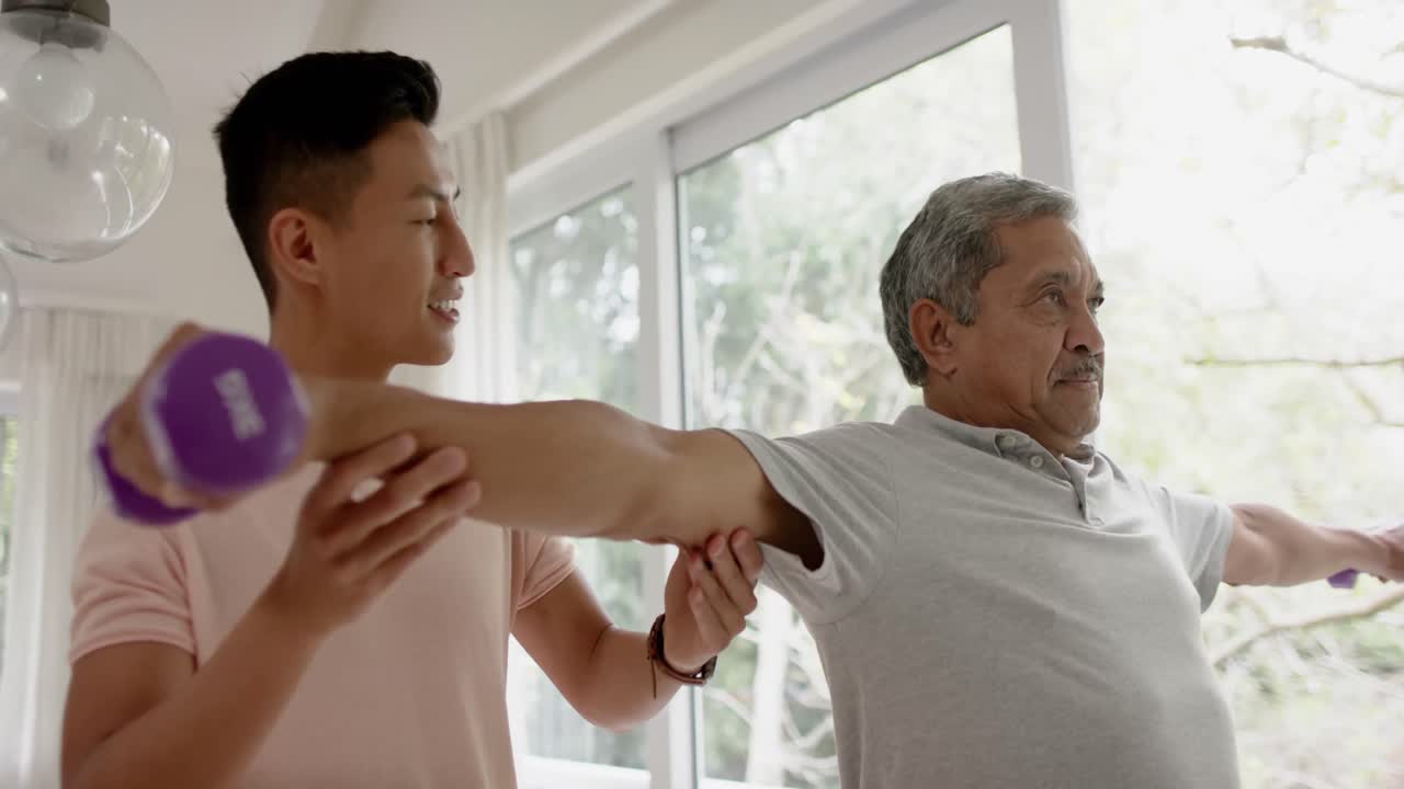 다양한 남성 물리치료사가 조언하고 단호한 고령자가 덤벨을 사용하여 느린 동작으로