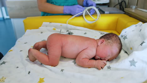 naked newborn kid lies on the belly. neonatologist uses stethoscope to examine health of a baby.