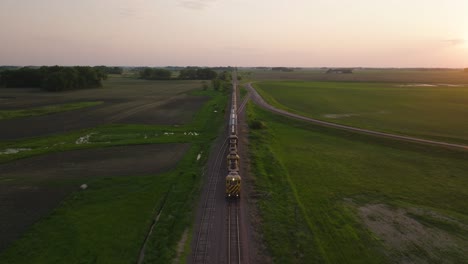 aerial view of freight train running through the countryside fields at dusk