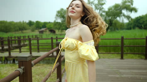 feminine young woman wearing yellow sundress walking down park boardwalk twirling and looking at camera - slow motion