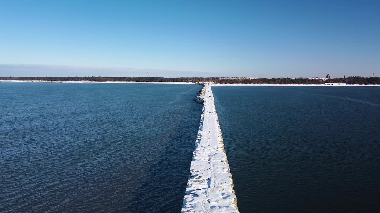 vista aérea del muelle de hormigón cubierto de nieve y hielo en el tranquilo mar báltico, puerto de liepaja en un soleado día de invierno, disparo de drones ascendentes de gran angular