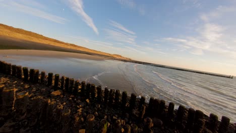 Schnelle-Tiefwinkelansicht-über-Einem-Deich-Und-Einem-Strand-Mit-Wellenbrechern-Bei-Ebbe