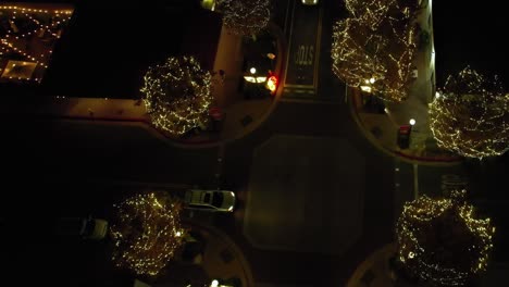 trees illuminated with christmas lights on quiet crossroad junction at night, aerial birdseye view