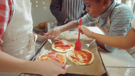 children spreading sauce on dough before baking on cooking masterclass