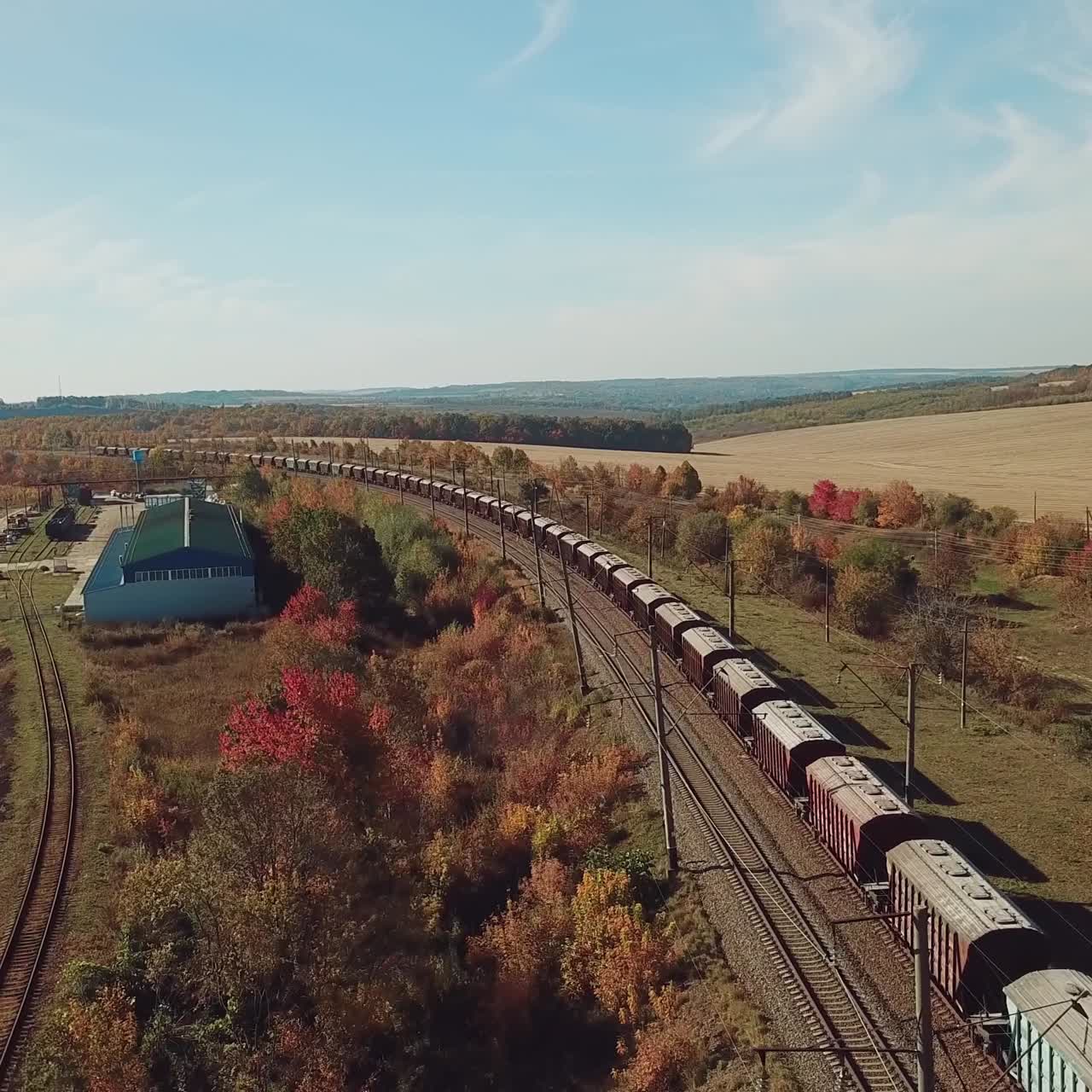 freight train is moving by rail to the nearest town on the background of the countryside with fields and road. Aerial view