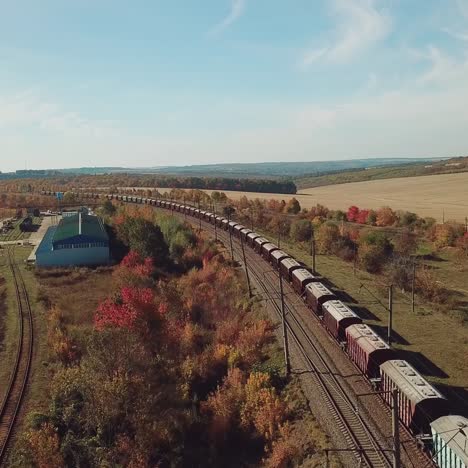 freight train is moving by rail to the nearest town on the background of the countryside with fields and road. aerial view