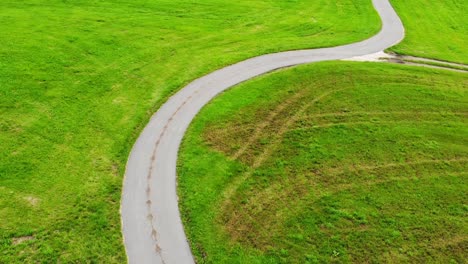 aerial view revealing curvy alpine road between green fields