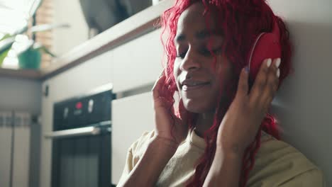 peaceful african ethnicity young woman wearing headphones, listening music at kitchen floor