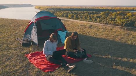 girlfriends-work-on-modern-tablet-and-laptop-sitting-by-tent