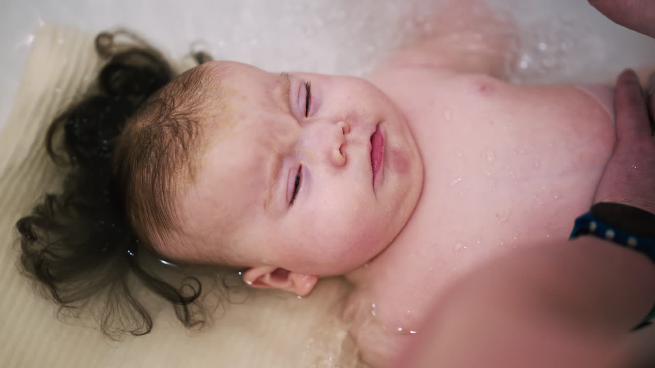 Baby lying in a bathtub enjoying bath time with caregiver support