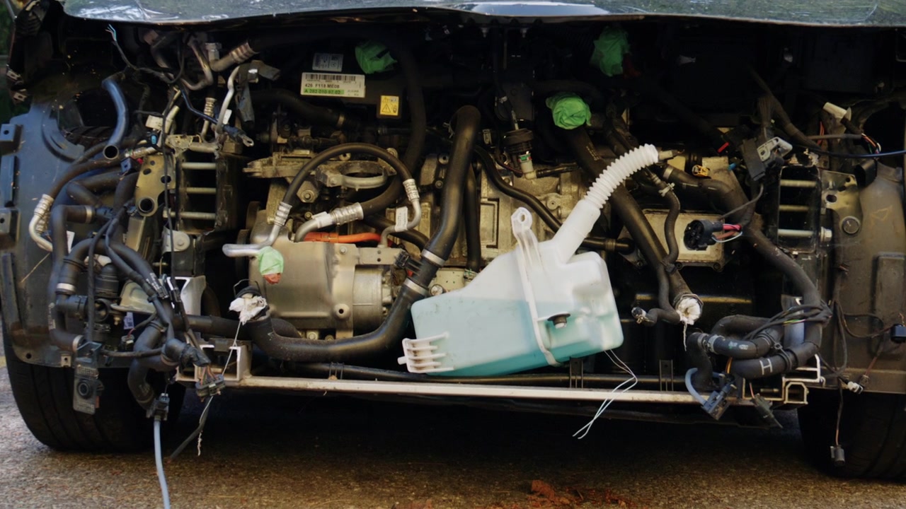 Detailed front view of a dismantled vehicle with exposed engine, hoses, wiring, and coolant container visible