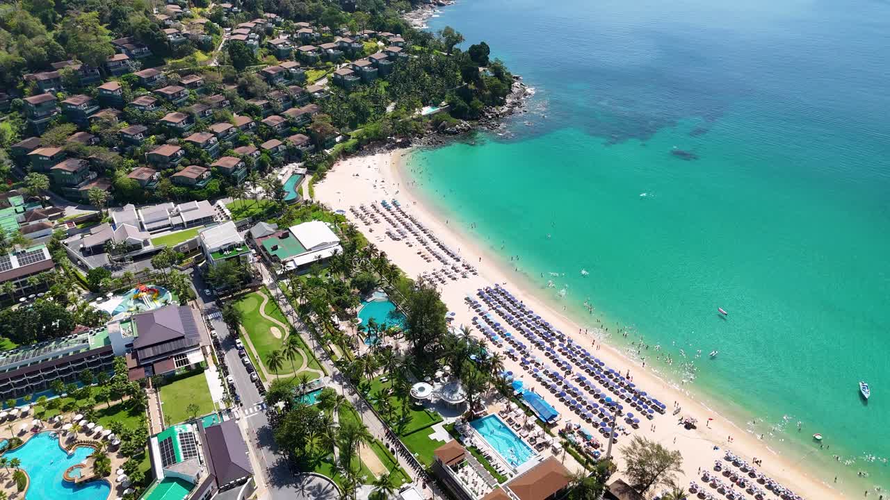 태국 푸켓에 있는 럭셔리 해변 리조트를 촬영한 공중 영상으로 빛 아래 푸른 물, 모래 해변, 울창한 초록색을 보여준다.