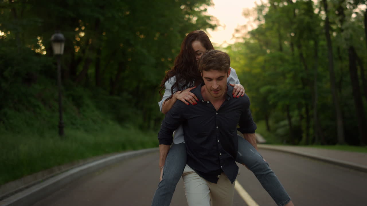 Young man piggyback woman on romantic date in summer park at sunset.