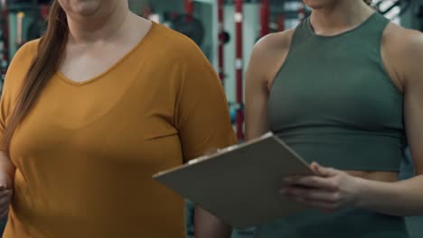 close up of overweight woman talking with female trainer in the gym.