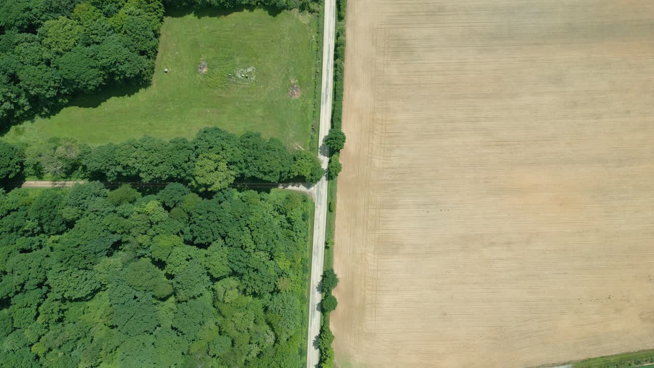 화창한 날 프랑스 노르망디의 도로를 따라 시골 한가운데 들판 위로 날아가는 드론의 4k 영화적 자연 영상