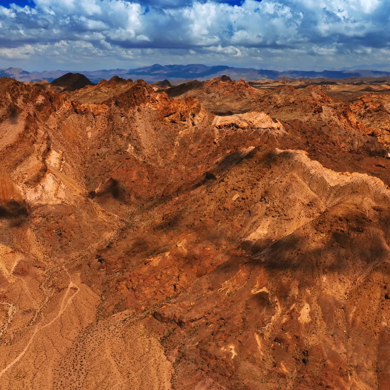 Shadows from clouds moving by the bare rock tops. Brown scenery of mountains in Mojave desert under the cloudy sky. Top view