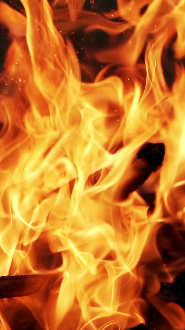 Wooden stick is mixing logs in bright fire. Orange flame from burning firewood outdoors. Smoldered logs in vivid fire flame. Vertical video