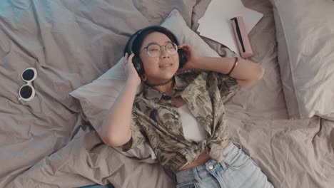 asian teenage girl enjoying music in headphones in bed