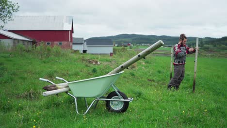 man in countryside removing fence pole and placed into wheelbarrow