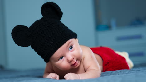nice healthy boy in funny mouse hat lies on his belly. beautiful child in red shorts keeps head up. close up. grey backdrop.