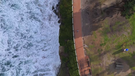 la jolla cove drone disparado de arriba hacia abajo dividido sobre las olas que se estrellan mientras la persona camina por el camino del parque desde la parte superior del cuadro hasta la parte inferior