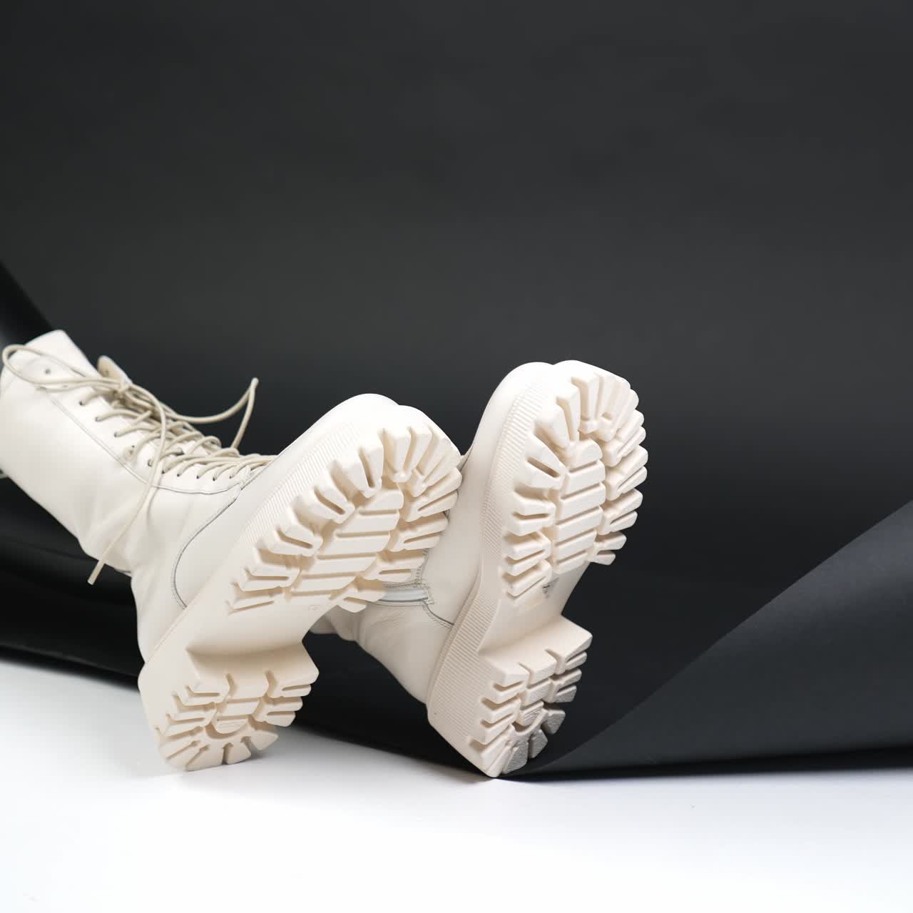 Legs of a model wearing white tractor soles boots. Female sitting on the floor in studio demonstrating modern stylish footwear