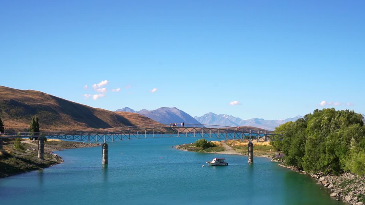 Poeple standing on bridge in Lake Tekapo, New Zealand with mountains in background