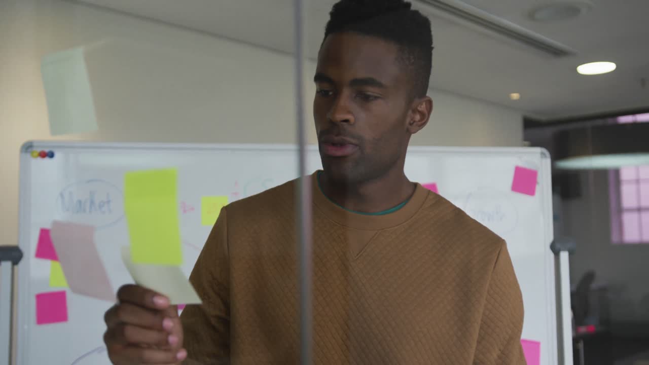 African american businessman standing behind glass wall in meeting room using sticky notes