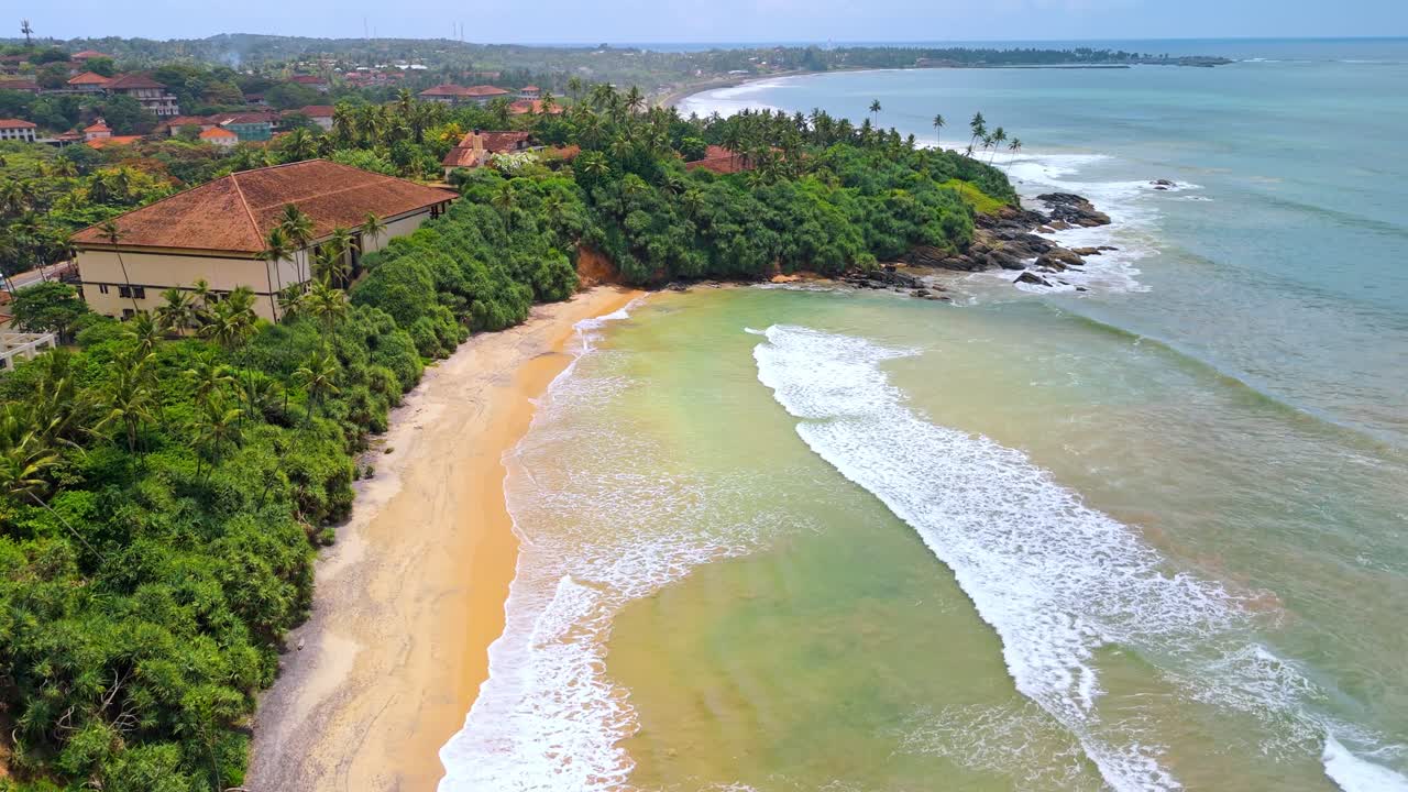 A breathtaking aerial drone shot of SK Town Surf Beach in Weligama, Sri Lanka, where lush jungle meets the ocean.