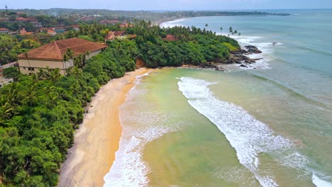 a breathtaking aerial drone shot of sk town surf beach in weligama, sri lanka, where lush jungle meets the ocean.