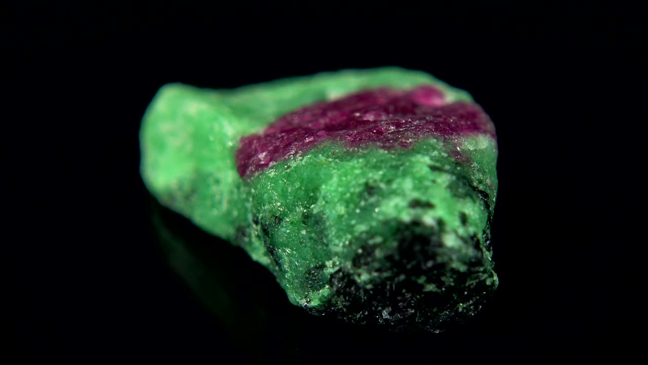 검은색 배경 앞에 보라색과 녹색의 미네랄 (루빈) 을 원활하게 회전시키는 것