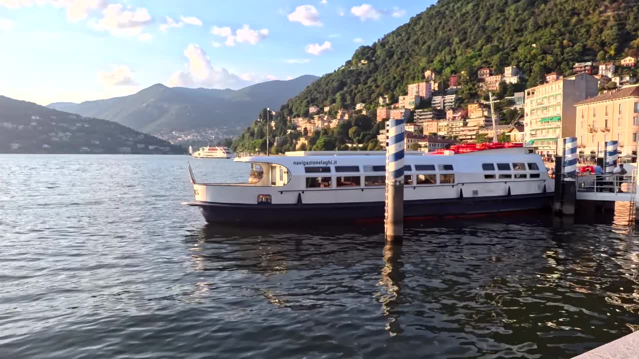 A scenic view of the pier in Lake Como of a stationary ship and the hills behind in Lombardy, Italy