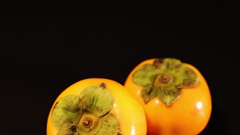 two persimmons rotating against a dark backdrop