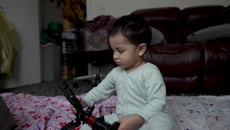 Adorable-18-month-old-baby,-joyfully-engages-with-a-camera-tripod,-exemplifying-the-essence-of-childhood-play-whilst-waving-at-television,-sitting-on-the-floor