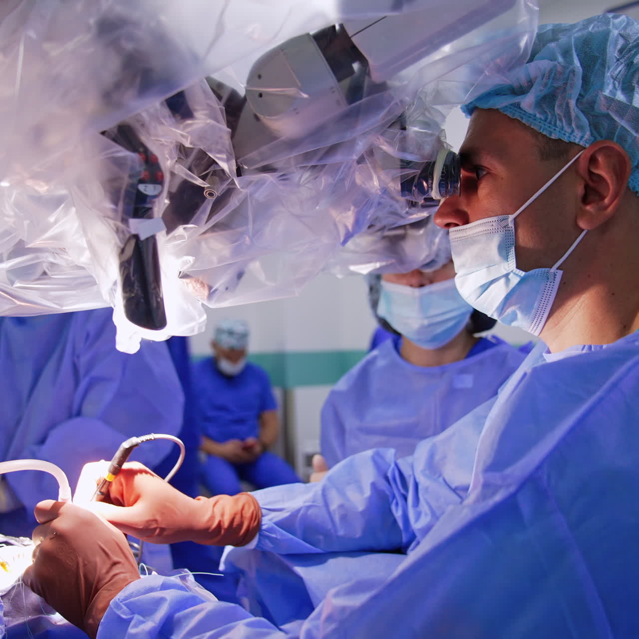 Caucasian male neurosurgeon carrying out the operation using microscope. Concentrated surgeon applies electric tools and devices. Side view.