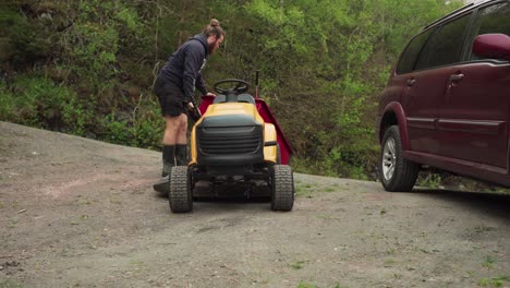 man detaching dump cart from lawn tractor parked next to an suv