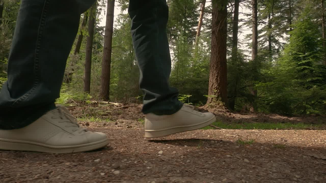 Closeup shot of a men steps in blue jeans and white shoes on a forest path