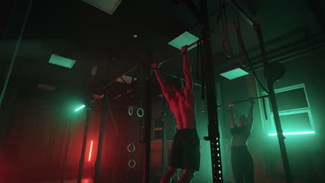 los atletas masculinos y femeninos están haciendo pull-up en la barra en el gimnasio entrenando duro
