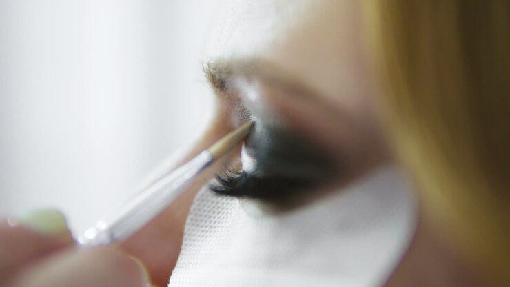 Makeup artist applying eyeshadow on eyelid using makeup brush and protecting skin with white patches. Professional makeup
