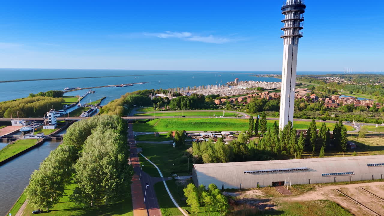 Amazing green waterscape of lake Markermeer in Lelystad. Drone flight approaches the telecom tower. Yacht club at backdrop. Aerial view.
